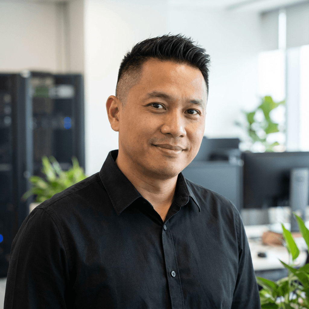 Smiling middle-aged Asian man in a black shirt standing in a bright, modern office.